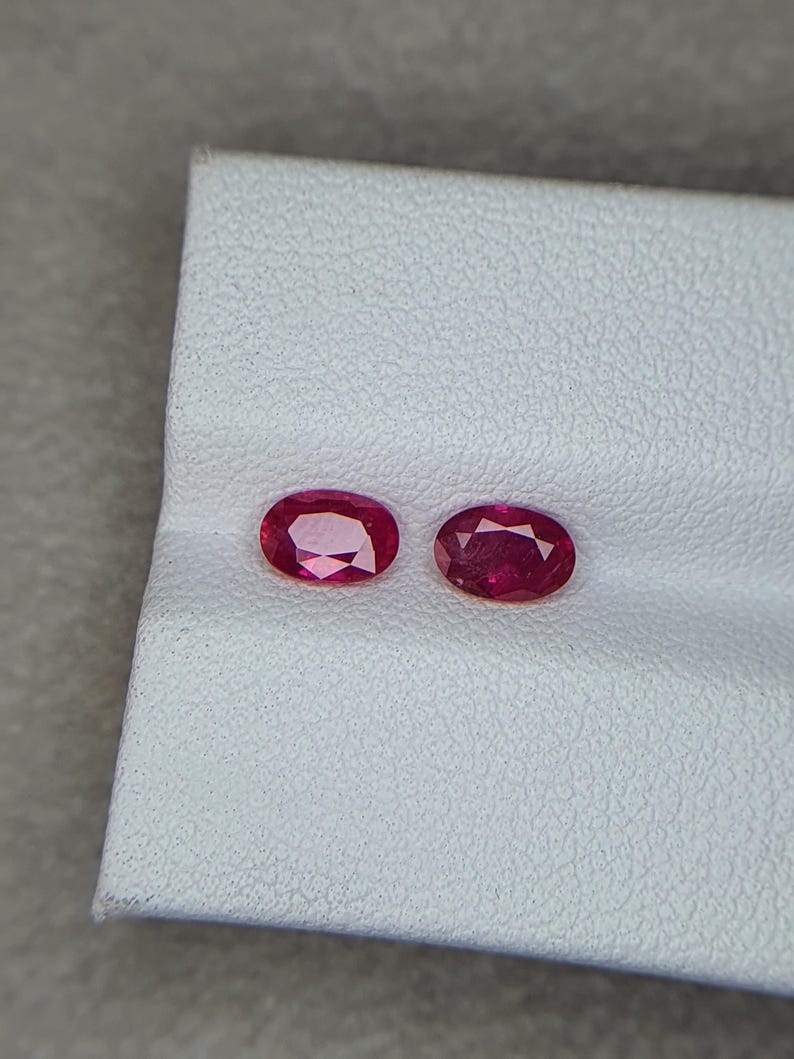 Op de afbeelding: Twee ovale, rode edelstenen op een witte achtergrond. De edelstenen zijn vergelijkbaar in grootte en vorm.