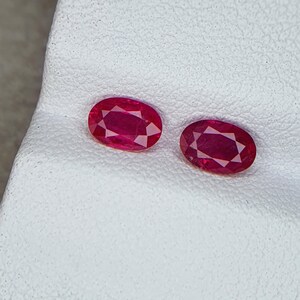 Op de afbeelding: Twee ovale, rode edelstenen op een wit oppervlak.