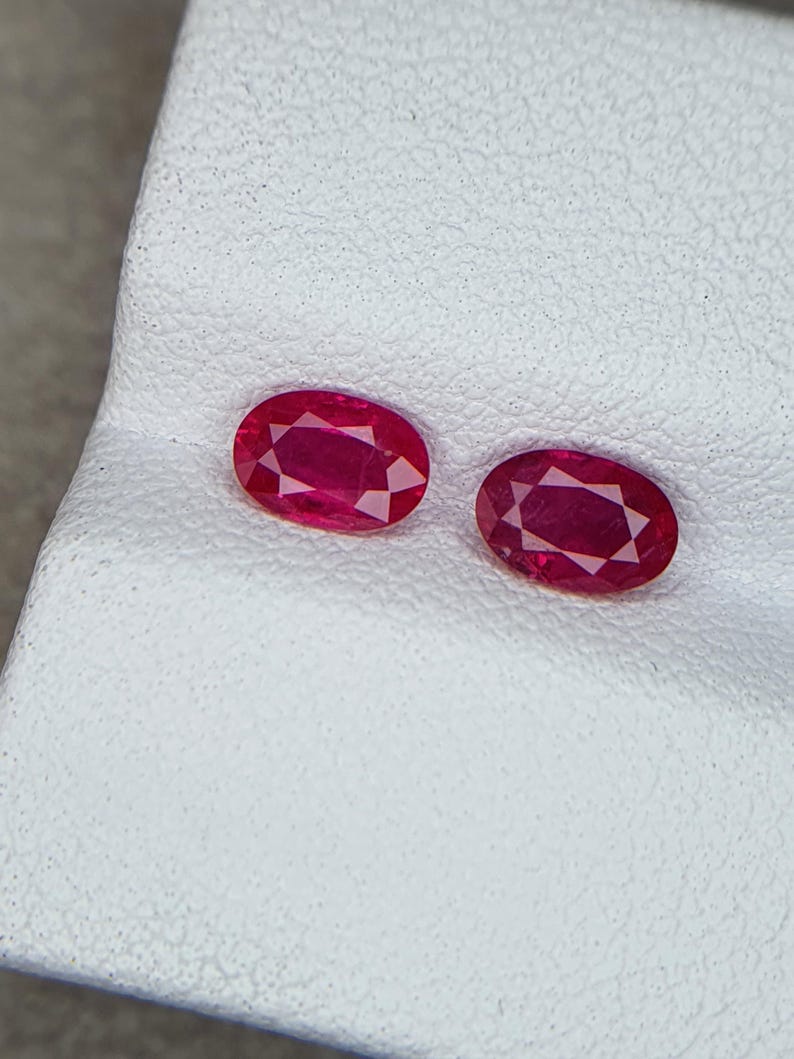 Op de afbeelding: Twee ovale, rode edelstenen op een wit oppervlak.