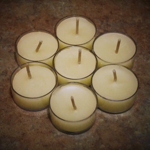 May include: Seven round, clear glass tea light holders with a white wax candle inside each one. The candles are arranged in a circle on a brown surface.