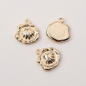 May include: Three gold-tone metal charms, two with a raised seashell design and one smooth and round.