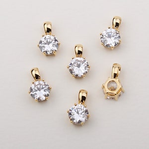Könnte beinhalten: Sechs goldfarbene Anhänger mit klaren Zirkonia-Steinen. Jeder Anhänger hat einen runden Stein mit einer Krappenfassung und einer Öse zum Anbringen an einer Kette.