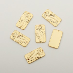 Op de afbeelding: Zes goudkleurige metalen bedels, vijf met een reliëfdesign van een paardenbloem, één is effen. De bedels zijn rechthoekig.