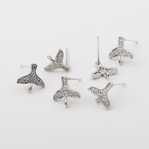 Könnte beinhalten: Fünf silberfarbene Ohrring-Verschlüsse mit einem klaren Kristall-Fischschwanz-Design. Jeder Verschluss hat einen Stift und eine Öse zum Anbringen eines Charms oder einer Perle.