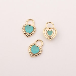 Puede incluir: Tres dijes dorados en forma de cerradura con forma de corazón y centros turquesa. Los dijes tienen un borde decorativo y un pequeño lazo en la parte superior. El fondo es blanco liso.