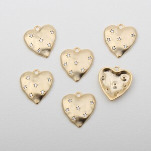 May include: Six gold heart-shaped charms with a textured surface and clear star-shaped rhinestones. The charms have a loop at the top for attaching to jewelry.