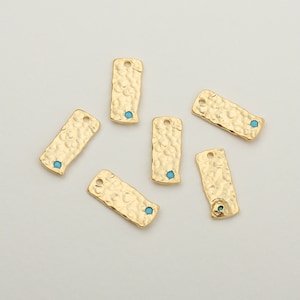 May include: Six gold-toned metal rectangular charms with a textured surface and a small turquoise blue stone in the centre of each charm.