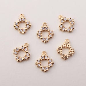 以下が含まれることがあります： クリアなラインストーンのアクセントが付いたゴールドトーンの金属製チャーム6個。各チャームは、中央に円形の開口部のある正方形の形をしています。