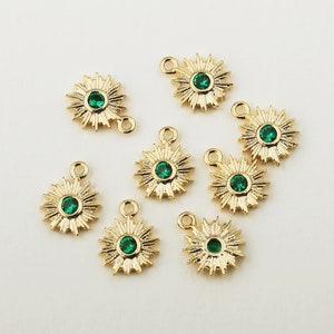 May include: Eight gold star-shaped charms with green gemstone centers. Each charm has a loop for attaching to jewelry.