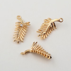 Könnte beinhalten: Drei goldene Palmenblatt-Anhänger mit einem klaren Strassstein-Akzent. Die Anhänger haben eine Öse oben zum Anbringen an Schmuck.