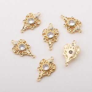 May include: Six gold-tone metal charms with clear rhinestone accents. Each charm features a decorative filigree design.