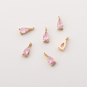 May include: Six gold-tone teardrop-shaped charms with pink crystal accents. The charms have a loop at the top for attaching to jewelry.