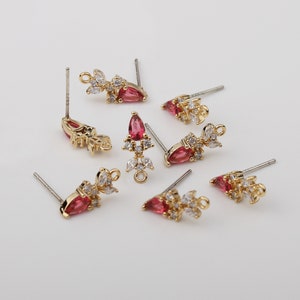 May include: Eight gold-tone earring findings with a teardrop-shaped red stone and clear rhinestones. The findings have a loop at the top for attaching a dangle charm.