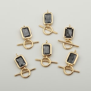 Peut inclure: Six fermoirs à bascule dorés avec des pierres rectangulaires noires. Chaque fermoir a un anneau et une barre.