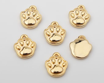 May include: Six gold-colored metal charms in the shape of a paw print. The charms have a smooth, shiny finish.