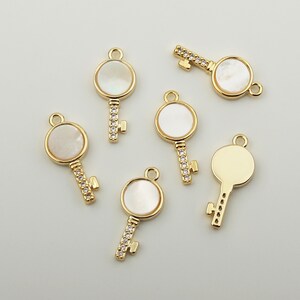 May include: Six gold key charms with white mother of pearl inlays. The keys have clear rhinestone accents.