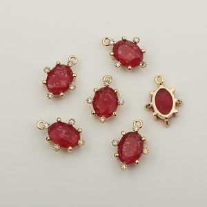 May include: Six gold-tone oval-shaped charms with red gemstone accents and clear crystal embellishments. Each charm has a loop for attaching to a necklace or bracelet.