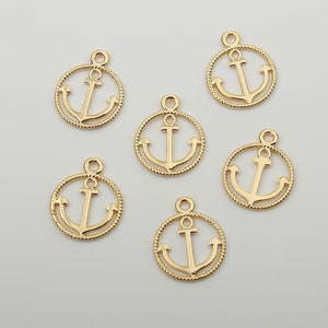 Op de afbeelding: Zes gouden metalen ankerbedels met een touwachtige rand. De ankers zijn allemaal even groot en even gevormd.