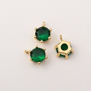 Könnte beinhalten: Drei goldfarbene Charms mit grünen Kristall-Akzenten. Jeder Charm verfügt über einen runden, facettierten Kristall mit einer goldfarbenen Fassung. Die Charms sind perfekt, um Schmuckprojekten einen Hauch von Glanz zu verleihen.