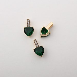 May include: Three gold heart-shaped pendants with green gemstones and clear crystal accents.