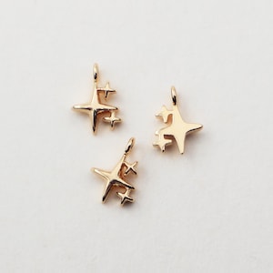 May include: Three gold-colored star charms with a polished finish. Each charm features a larger star with smaller stars clustered around it, and a small loop at the top for attaching to jewelry. The charms are ideal for crafting.
