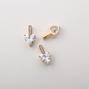 May include: Three gold heart-shaped pendants with clear cubic zirconia stones. Each pendant has a small row of clear cubic zirconia stones on the bail.