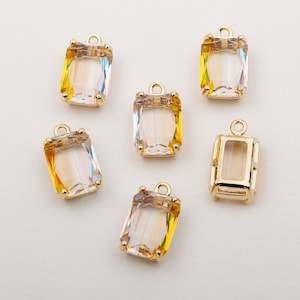 Puede incluir: Seis colgantes de tono dorado con piedras de vidrio rectangulares transparentes e iridiscentes. Las piedras tienen un tono amarillo sutil.