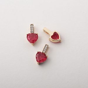 May include: Three gold heart-shaped charms with red glitter accents and clear crystal accents. The charms have a loop at the top for attaching to a necklace or bracelet.