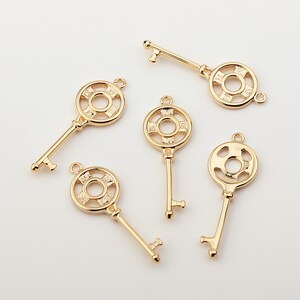 May include: Five gold-tone key charms with ornate circular designs. Each charm features a keyhole and a decorative circle with Roman numeral markings.