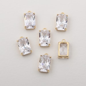 Puede incluir: Seis colgantes de tono dorado con piedras de circonita cúbica transparentes. Los colgantes tienen forma rectangular con esquinas redondeadas.