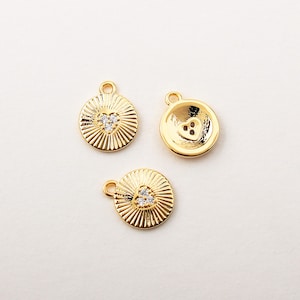 May include: Three gold-tone metal charms with a heart design. Each charm has a different design, one with a heart with a single rhinestone, one with a heart with three rhinestones, and one with a heart with a button design.