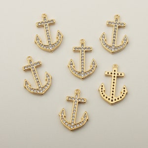 Op de afbeelding: Zes gouden ankerbedels met heldere kristallen accenten. De bedels zijn perfect voor het maken van sieraden of om een ​​nautische touch toe te voegen aan ambachten.