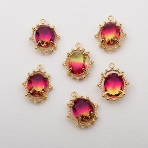 May include: Six gold-tone pendant charms with a red, yellow, and green ombre oval-shaped glass stone in the centre. Each charm has a decorative, scalloped, gold-tone frame.