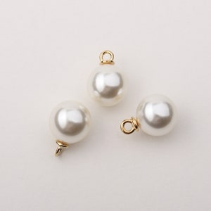 May include: Three white pearl beads with gold loop attachments. The beads are round and smooth.