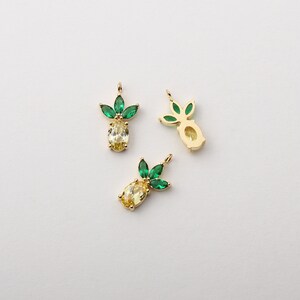 Puede incluir: Tres abalorios de piña dorados con hojas de cristal verde. Las piñas tienen un centro de cristal amarillo.