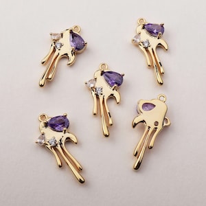 May include: Five gold-tone pendant charms with a dripping paint design. Each charm features a purple gemstone and clear rhinestones.