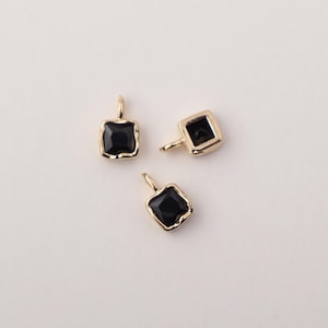 May include: Three gold charms with black square-shaped stones. The charms have a loop at the top for attaching to a necklace or bracelet.