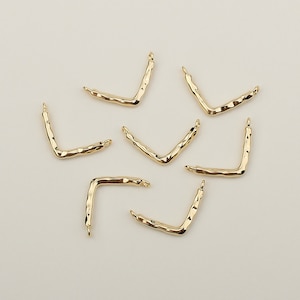 May include: A set of six gold-toned metal V-shaped connectors. The connectors are textured and have a slightly irregular shape.