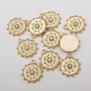 May include: A set of ten gold-toned metal charms with a circular design. Each charm features a raised, ornate pattern and a small, iridescent opal-like stone in the center. The charms have a loop at the top for attaching to jewelry or other crafts.