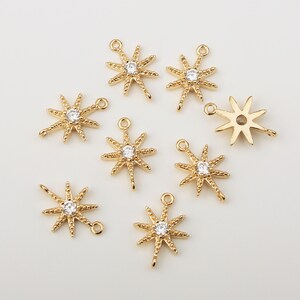 Peut inclure: Huit breloques en forme d'étoile dorées avec un strass transparent au centre. Chaque breloque a deux boucles pour l'attacher à des bijoux.