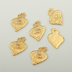 May include: Six gold-coloured metal charms in the shape of a heart with an eye design. The charms have a textured surface and are perfect for jewellery making.