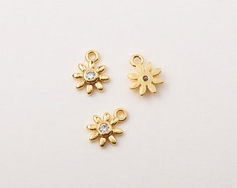 May include: Three gold-toned flower charms with a clear rhinestone in the centre. Each charm has a loop at the top for attaching to jewellery.