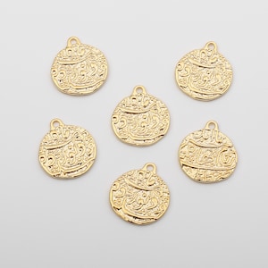 May include: Six gold-toned metal charms with intricate Arabic script designs. The charms are round and have a hole at the top for attaching to jewelry.