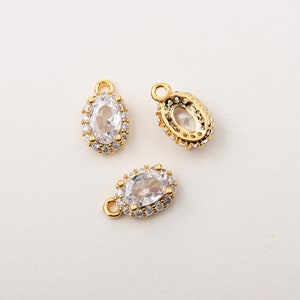 May include: Three gold oval-shaped charms with clear cubic zirconia stones set in a pave setting. The charms have a loop at the top for attaching to jewellery.