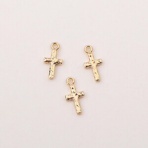 May include: Three gold-toned cross charms with a textured surface. The charms are perfect for adding a touch of faith to jewelry projects.