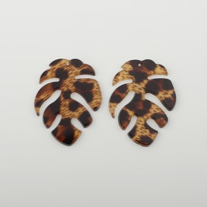 Könnte beinhalten: Zwei braune und schwarze Leopardenmuster-Monstera-Blatt-förmige Acryl-Ohrringe.