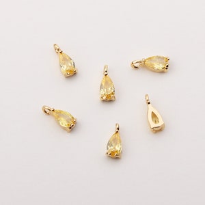 May include: Six small, gold-colored teardrop-shaped pendants with yellow gemstones. Each pendant has a small loop at the top for attaching to a chain or other jewelry component. The gemstones are a light yellow color.