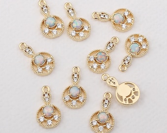 May include: Gold-toned pendant charms with opal-like center stones and clear crystal accents. Each charm features a circular design with a smaller, elongated top section for attachment. The charms are ideal for jewelry making.