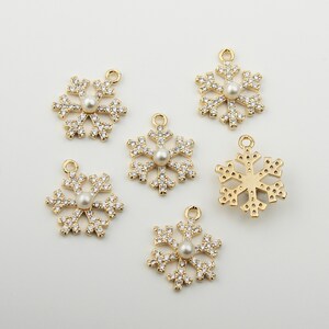 May include: Six gold snowflake charms featuring clear rhinestones and a white pearl at the centre. The charms are ideal for jewellery making or adding a touch of sparkle to crafts.