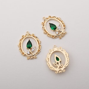 Puede incluir: Colgantes de joyería dorados con marcos ornamentados. Cada colgante presenta una gema verde central en forma de lágrima, con gemas blancas más pequeñas y un diseño floral. Los colgantes están diseñados para la fabricación de joyas.